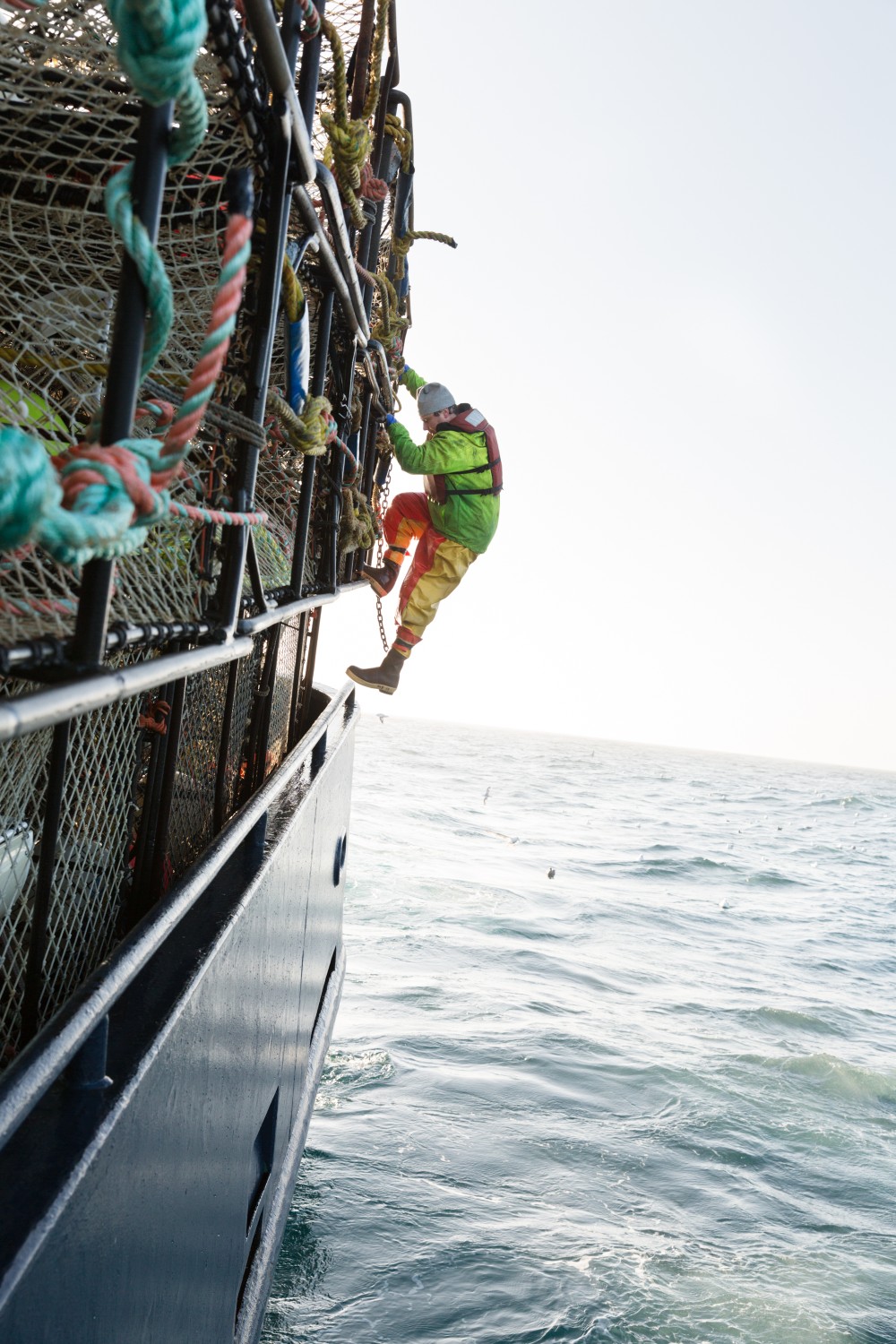 Alaskan Fisherman crew member climbing the side of the boat past stacked crab pots, with the calm sea on the horizon