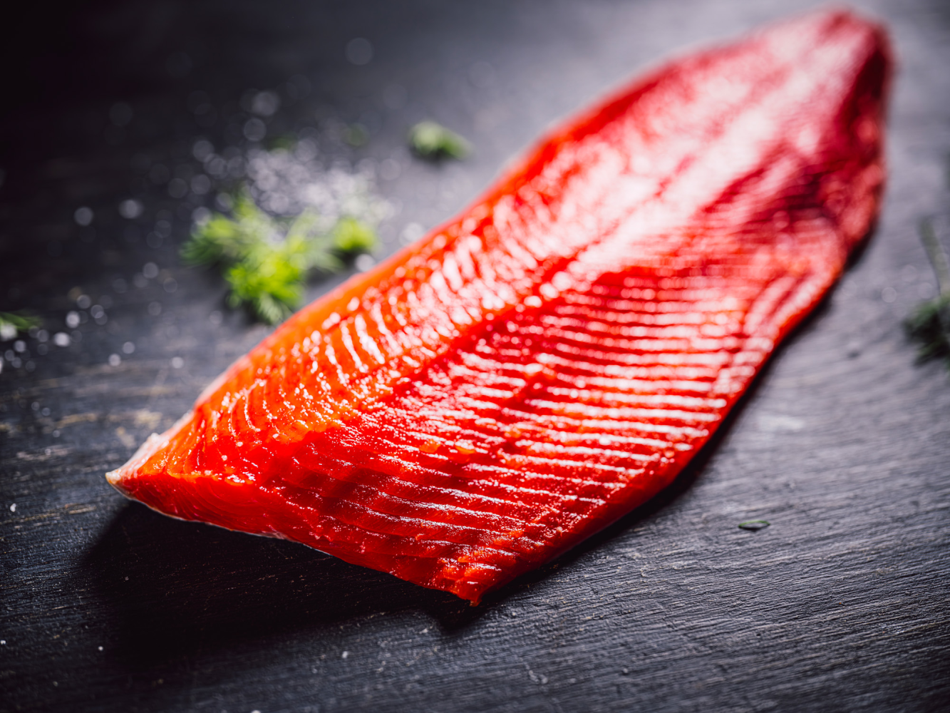 Vivid red wild salmon fillet on a dark surface, garnished with dill and salt