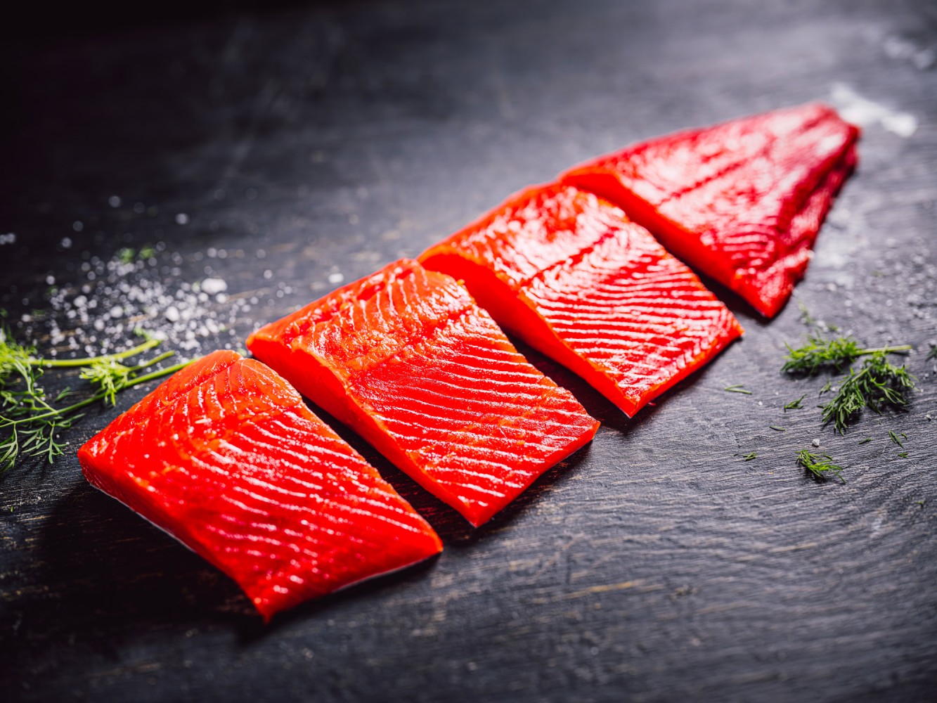 Four portions of wild salmon arranged on a dark surface